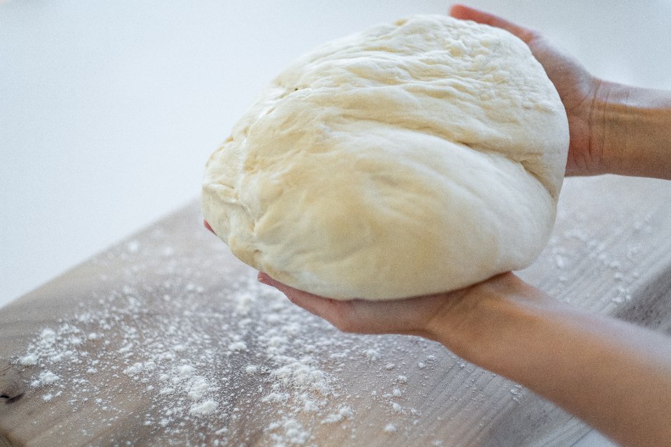 Hands holding a ball of bread dough over a floured board